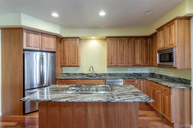 kitchen featuring dark stone counters, recessed lighting, light wood-style flooring, stainless steel appliances, and a sink