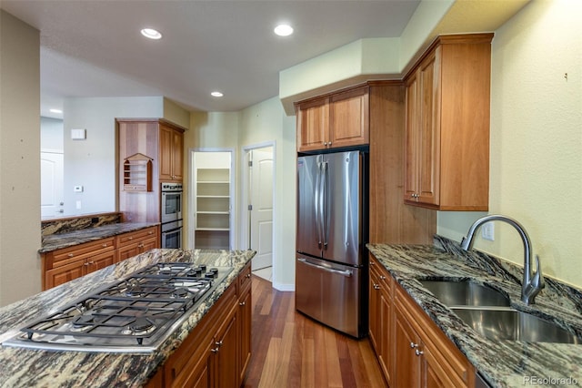 kitchen with a sink, dark stone countertops, brown cabinets, stainless steel appliances, and dark wood-style flooring