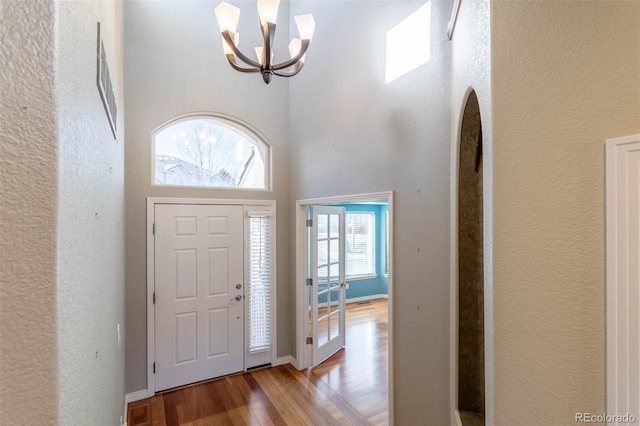 foyer entrance with an inviting chandelier, wood finished floors, baseboards, and a towering ceiling