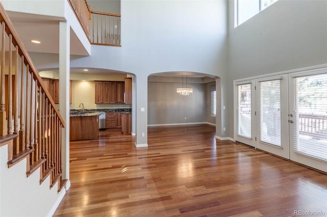 unfurnished living room featuring light wood finished floors, baseboards, an inviting chandelier, arched walkways, and a sink