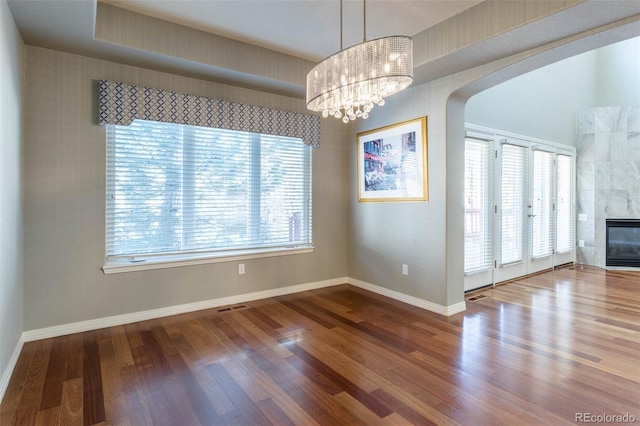 unfurnished dining area featuring wood finished floors, visible vents, baseboards, a fireplace, and arched walkways