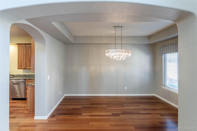 unfurnished dining area featuring light wood finished floors, a notable chandelier, arched walkways, and baseboards