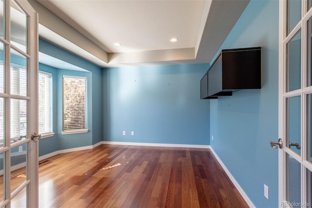 spare room featuring a tray ceiling, wood finished floors, recessed lighting, french doors, and baseboards