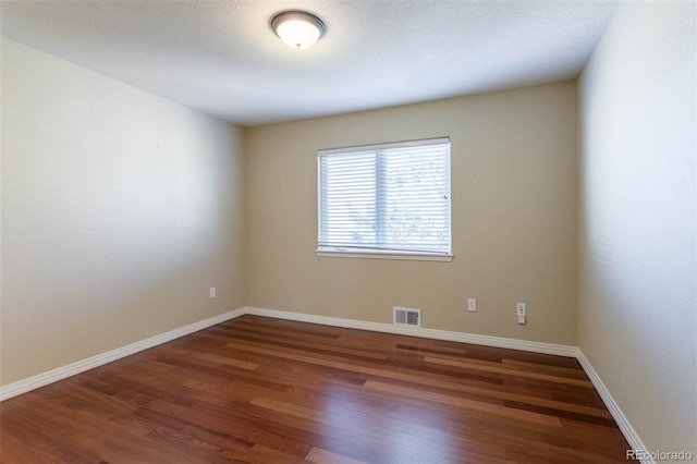 empty room featuring wood finished floors, visible vents, and baseboards