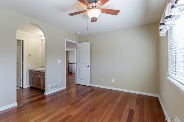 empty room featuring baseboards, arched walkways, wood finished floors, and a ceiling fan