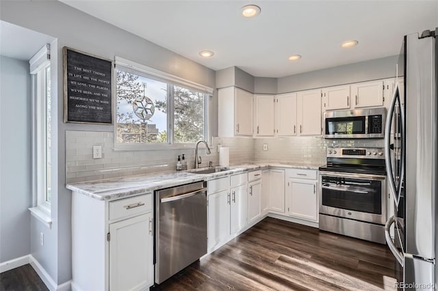 kitchen featuring light stone countertops, white cabinets, appliances with stainless steel finishes, and a sink