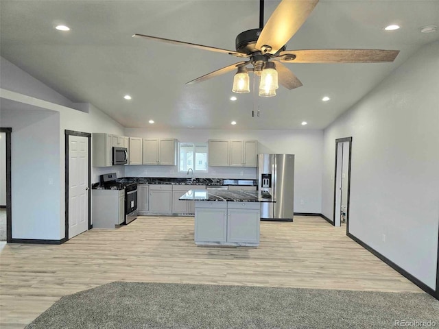 kitchen with appliances with stainless steel finishes, dark stone counters, sink, a kitchen island, and lofted ceiling