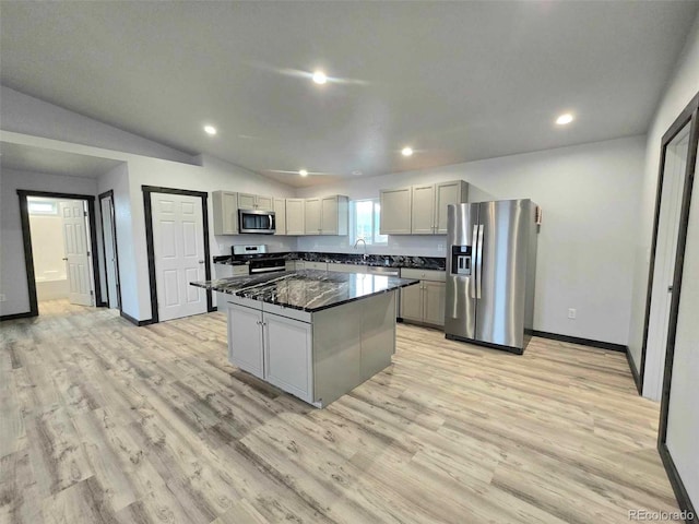 kitchen with dark stone counters, gray cabinetry, stainless steel appliances, vaulted ceiling, and a kitchen island