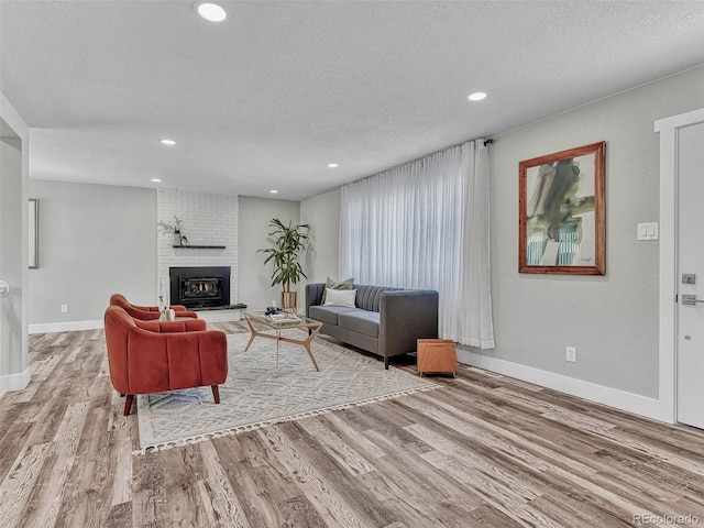 living room featuring light hardwood / wood-style floors, a textured ceiling, and a brick fireplace