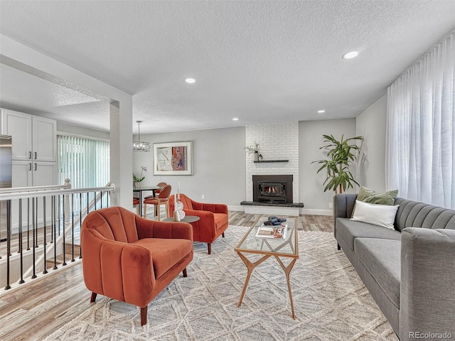 living room with a fireplace, a textured ceiling, light hardwood / wood-style flooring, and a notable chandelier