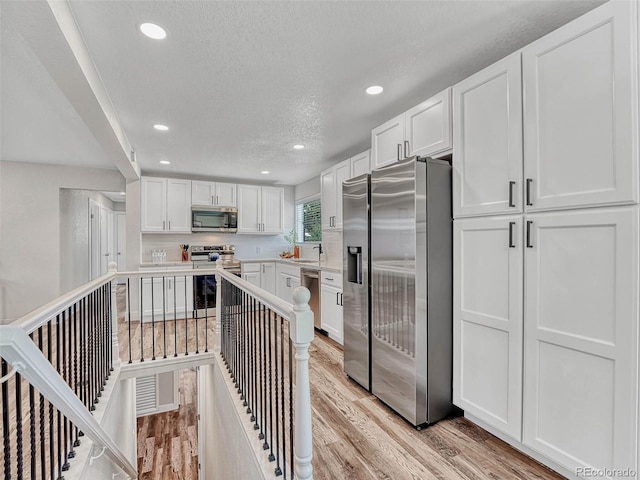 kitchen with decorative backsplash, white cabinets, stainless steel appliances, and light hardwood / wood-style floors