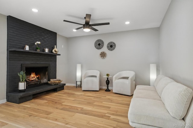 living room featuring ceiling fan, light wood-type flooring, and a fireplace