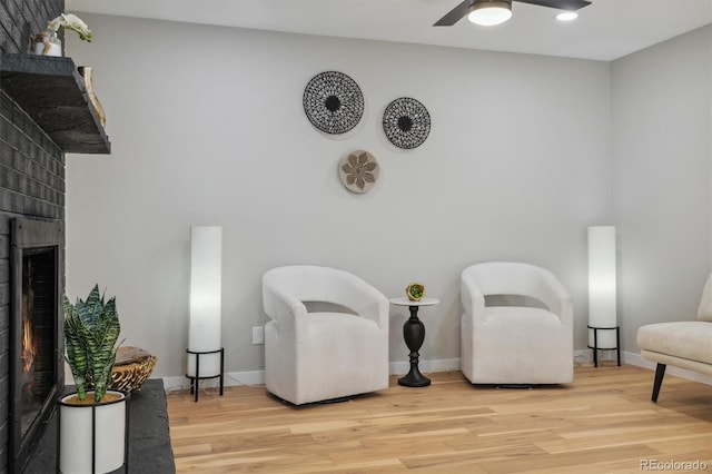 living area featuring a brick fireplace, ceiling fan, and light hardwood / wood-style floors