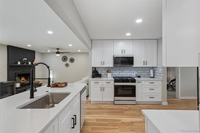 kitchen featuring white cabinets, a fireplace, light wood-type flooring, stainless steel appliances, and sink