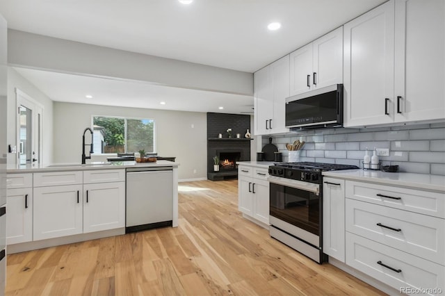 kitchen featuring light wood-type flooring, a fireplace, white cabinetry, stainless steel appliances, and sink