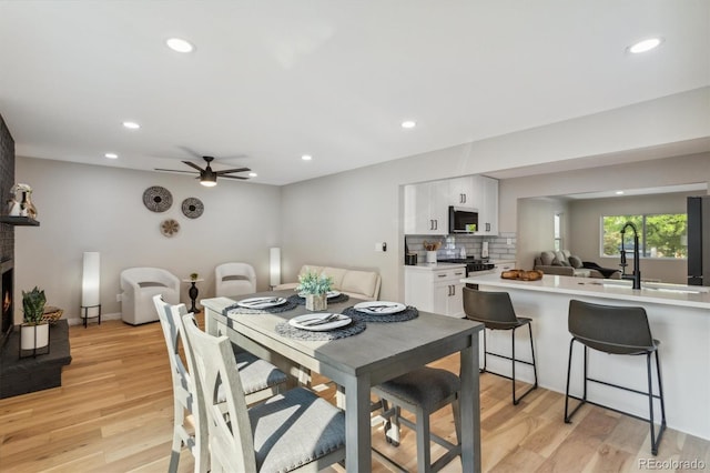 dining space featuring light wood-type flooring, sink, ceiling fan, and a large fireplace