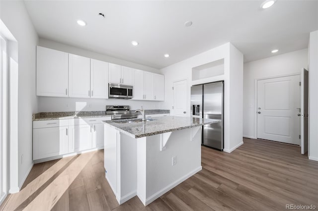 3889 N Shawee St, Aurora, CO 80019 - kitchen with appliances with stainless steel finishes, light wood-style floors, white cabinets, an island with sink, and light stone counters