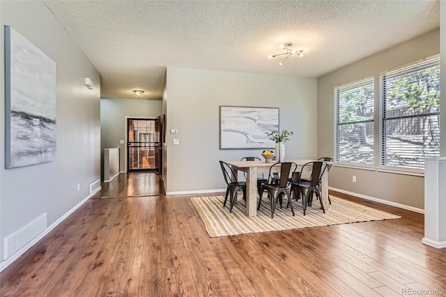 dining space with baseboards, visible vents, a textured ceiling, and hardwood / wood-style floors