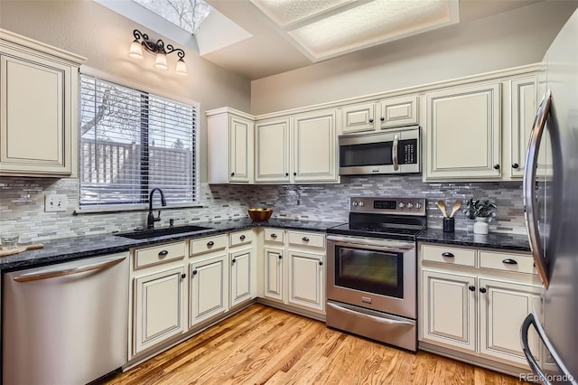 kitchen with a sink, light wood finished floors, a skylight, stainless steel appliances, and cream cabinetry