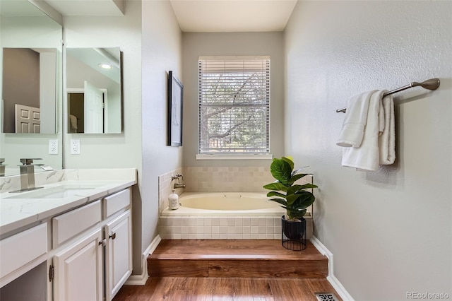 full bathroom featuring baseboards, wood finished floors, vanity, and a garden tub