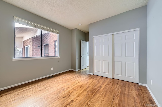 unfurnished bedroom with a closet, a textured ceiling, visible vents, baseboards, and wood finished floors