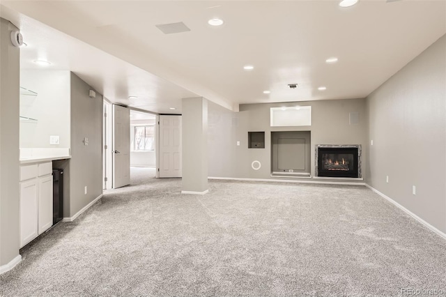unfurnished living room with light carpet, a glass covered fireplace, baseboards, and recessed lighting