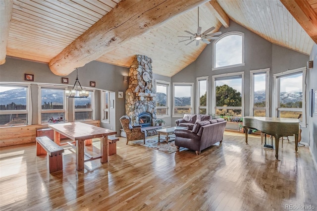 interior space with a stone fireplace, ceiling fan with notable chandelier, lofted ceiling with beams, a mountain view, and wooden ceiling