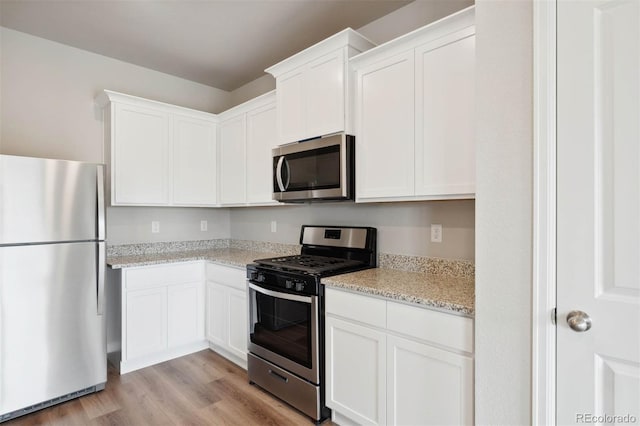 kitchen featuring light stone counters, white cabinetry, appliances with stainless steel finishes, and light hardwood / wood-style flooring