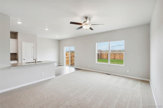 unfurnished living room featuring ceiling fan, sink, and light colored carpet