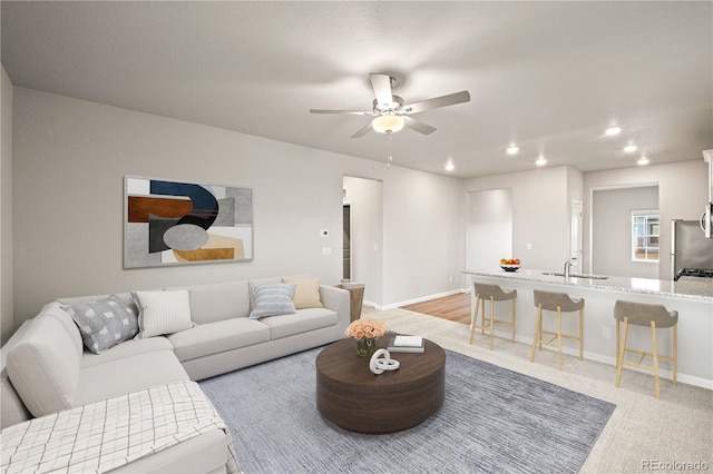 carpeted living room featuring ceiling fan and sink