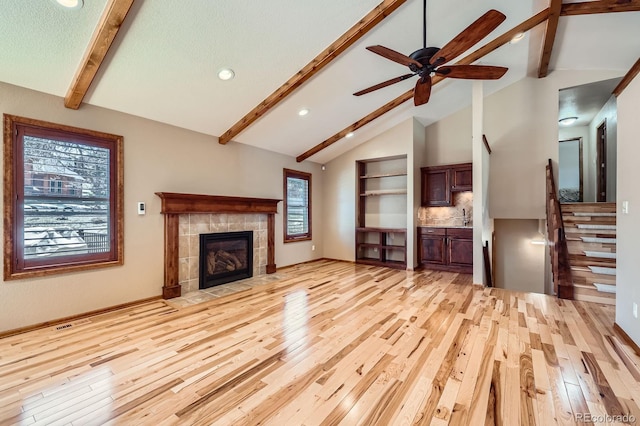 unfurnished living room with light wood-style floors, beamed ceiling, a tiled fireplace, and plenty of natural light