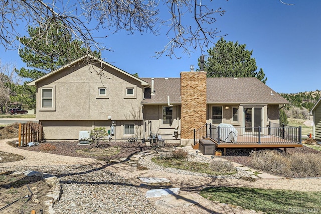 back of property with a chimney, a deck, roof with shingles, and stucco siding