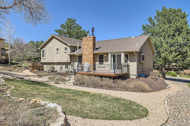 rear view of property with a deck, stucco siding, a chimney, and a shingled roof