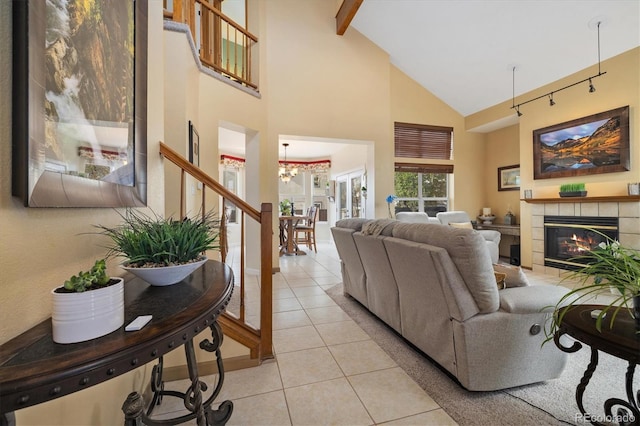 living area with a tiled fireplace, beam ceiling, light tile patterned floors, high vaulted ceiling, and stairs