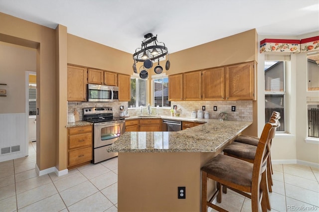 kitchen with appliances with stainless steel finishes, a sink, a peninsula, light tile patterned floors, and visible vents