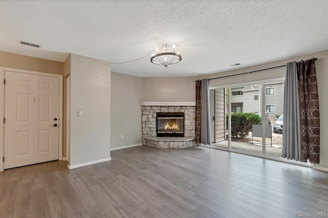 unfurnished living room with a fireplace, an inviting chandelier, hardwood / wood-style flooring, and a textured ceiling