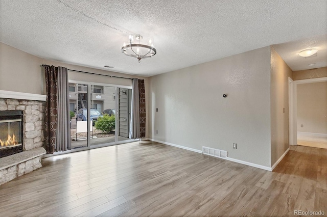 unfurnished living room featuring a textured ceiling, a notable chandelier, light wood-type flooring, and a stone fireplace