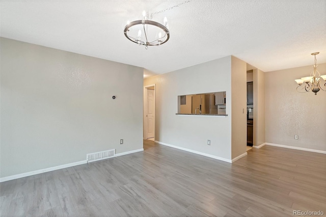 spare room with sink, hardwood / wood-style floors, an inviting chandelier, and a textured ceiling