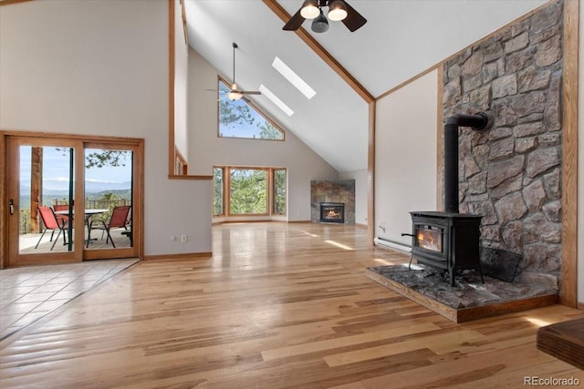 unfurnished living room with a wood stove, wood finished floors, ceiling fan, and high vaulted ceiling