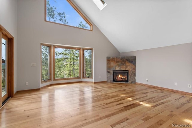 unfurnished living room with high vaulted ceiling, a fireplace, a skylight, light wood-type flooring, and baseboards