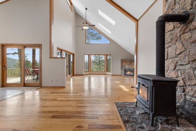 unfurnished living room featuring light wood-style flooring, high vaulted ceiling, a tiled fireplace, ceiling fan, and a wood stove