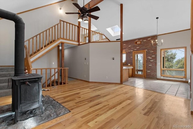 unfurnished living room featuring ceiling fan, high vaulted ceiling, wood finished floors, a wood stove, and a skylight