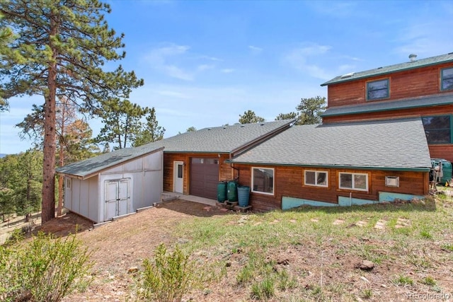 back of house with a storage shed, a shingled roof, an outdoor structure, and a garage