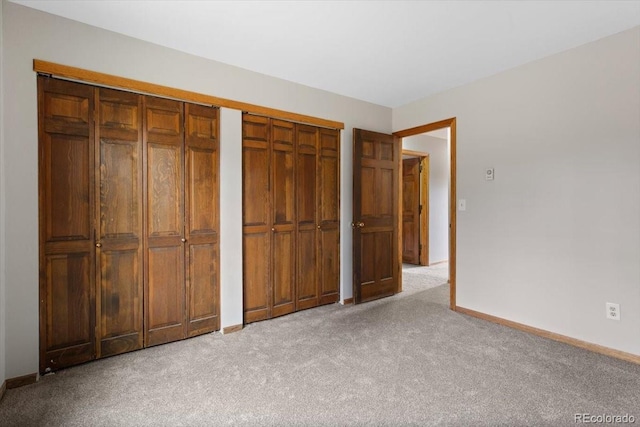 unfurnished bedroom with baseboards, two closets, and light colored carpet