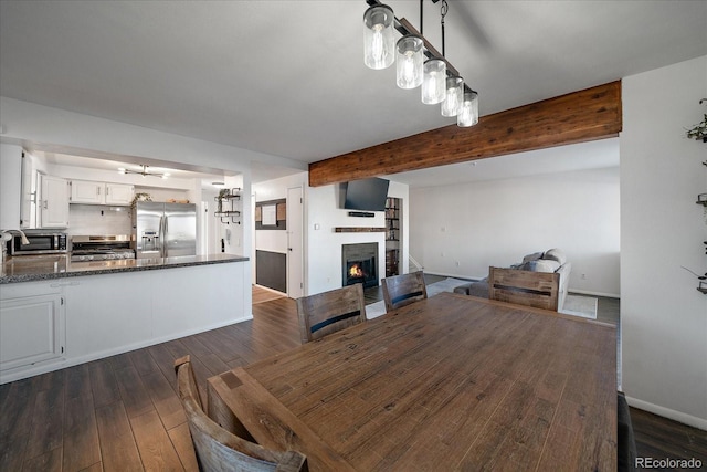 dining room featuring beam ceiling, dark hardwood / wood-style flooring, and a stone fireplace