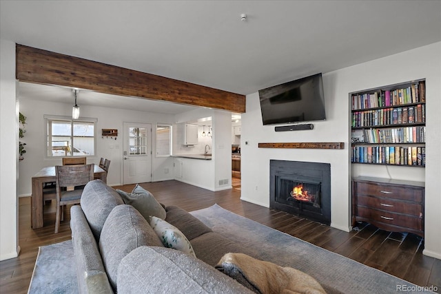 living room featuring beam ceiling, sink, and dark wood-type flooring