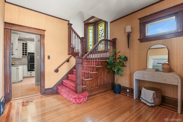 staircase with ornamental molding, baseboards, wood finished floors, and a healthy amount of sunlight