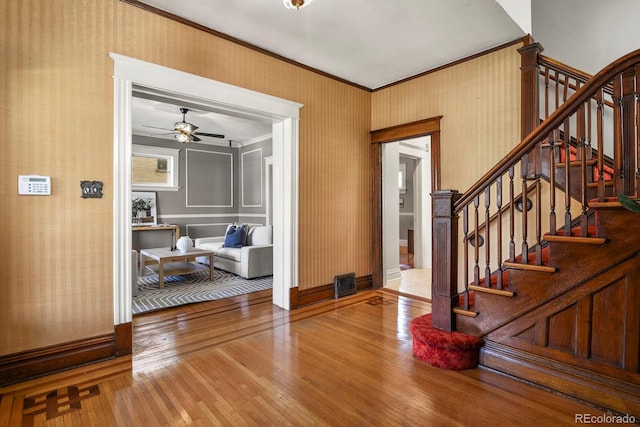 entrance foyer featuring ceiling fan, ornamental molding, hardwood / wood-style floors, stairs, and baseboards