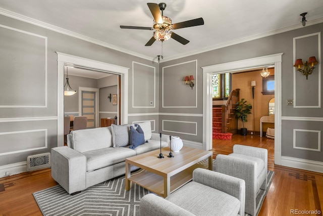 living room featuring visible vents, a decorative wall, a ceiling fan, crown molding, and wood finished floors