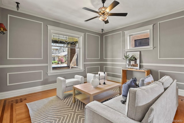 living area featuring wood finished floors, ornamental molding, baseboards, and a ceiling fan